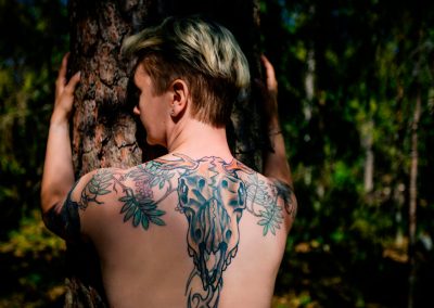 Tatuoitu nainen halaa puuta Järvenpään metsässä kesällä 2020